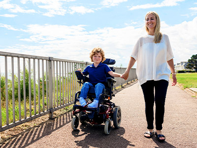 Young boy in motorized wheelchair holding hands with his mother