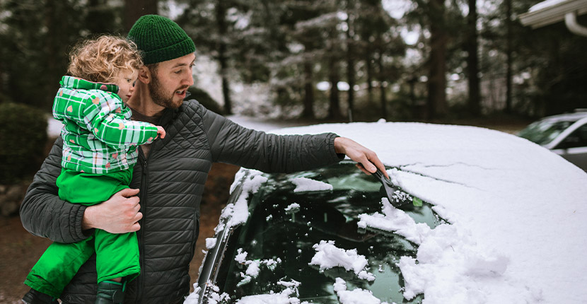 Father holding daughter while scraping off car window.